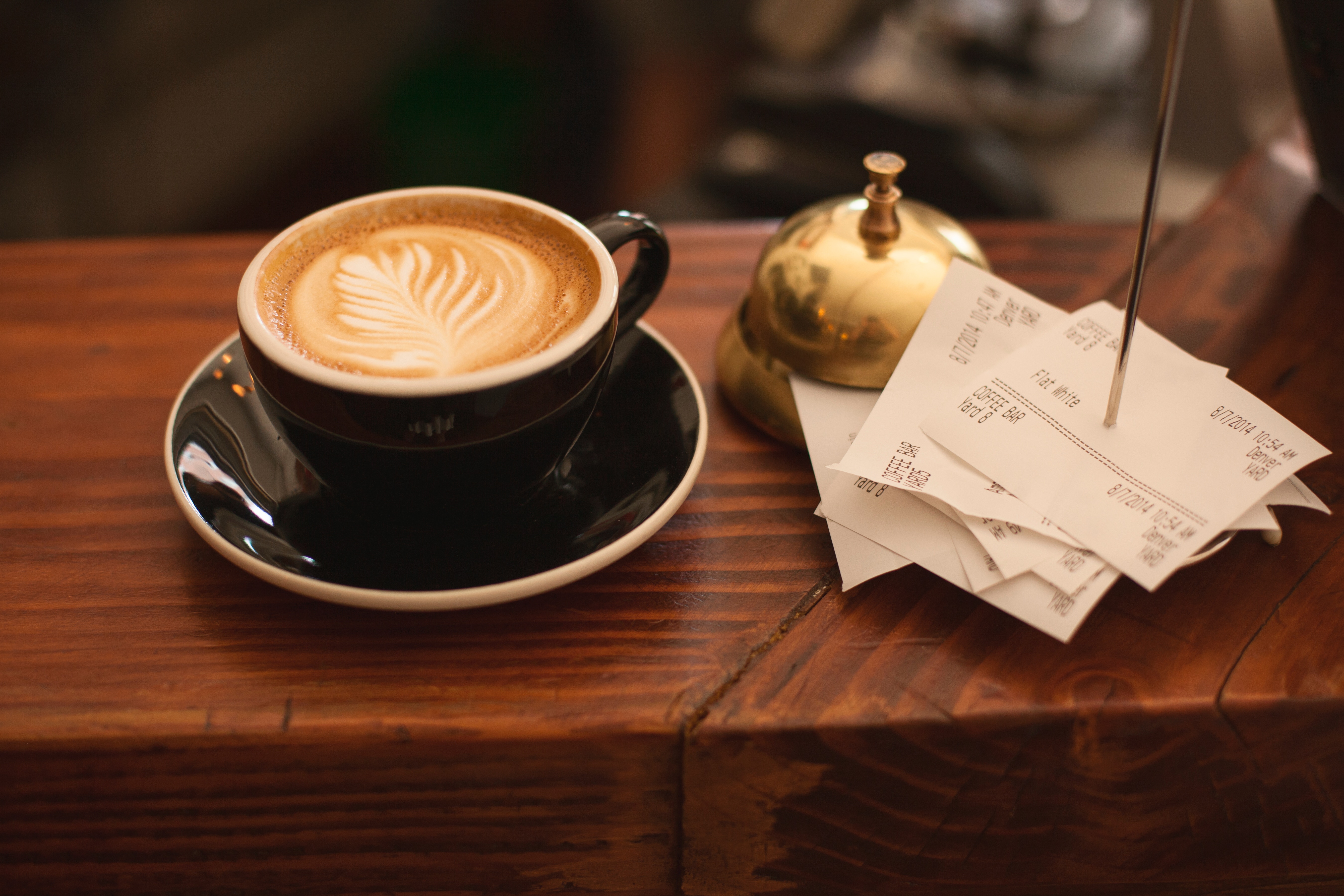 Cup of coffee on a table next to a stack of coffee shop receipts and a service bell