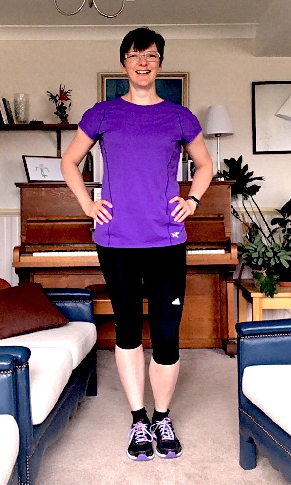 Cathy Worden showing off her runwear. She is wearing a purple t-shirt, running shorts, and matching running shoes.