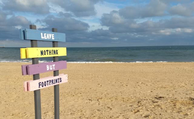 A sandy beach with a colourful sign saying 'Leave nothing but footprints'.