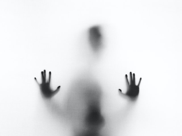 Blurry image of a person behind a clouded screen. Their hands are clear to see.