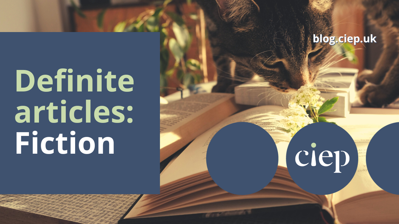 Header image with text Definite articles: fiction. Photo of cat sniffing a flower on a book.