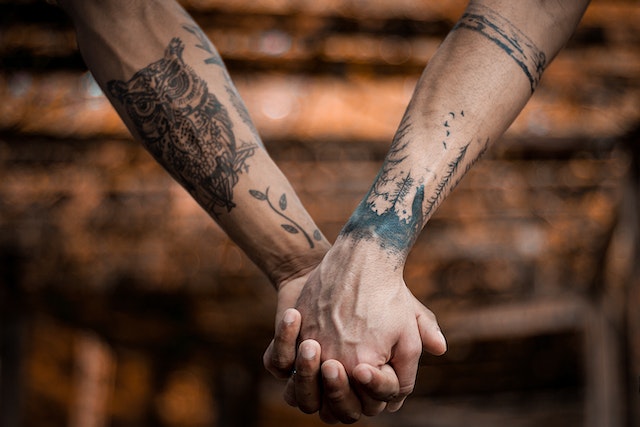 two people with tattoos on their arms hold hands